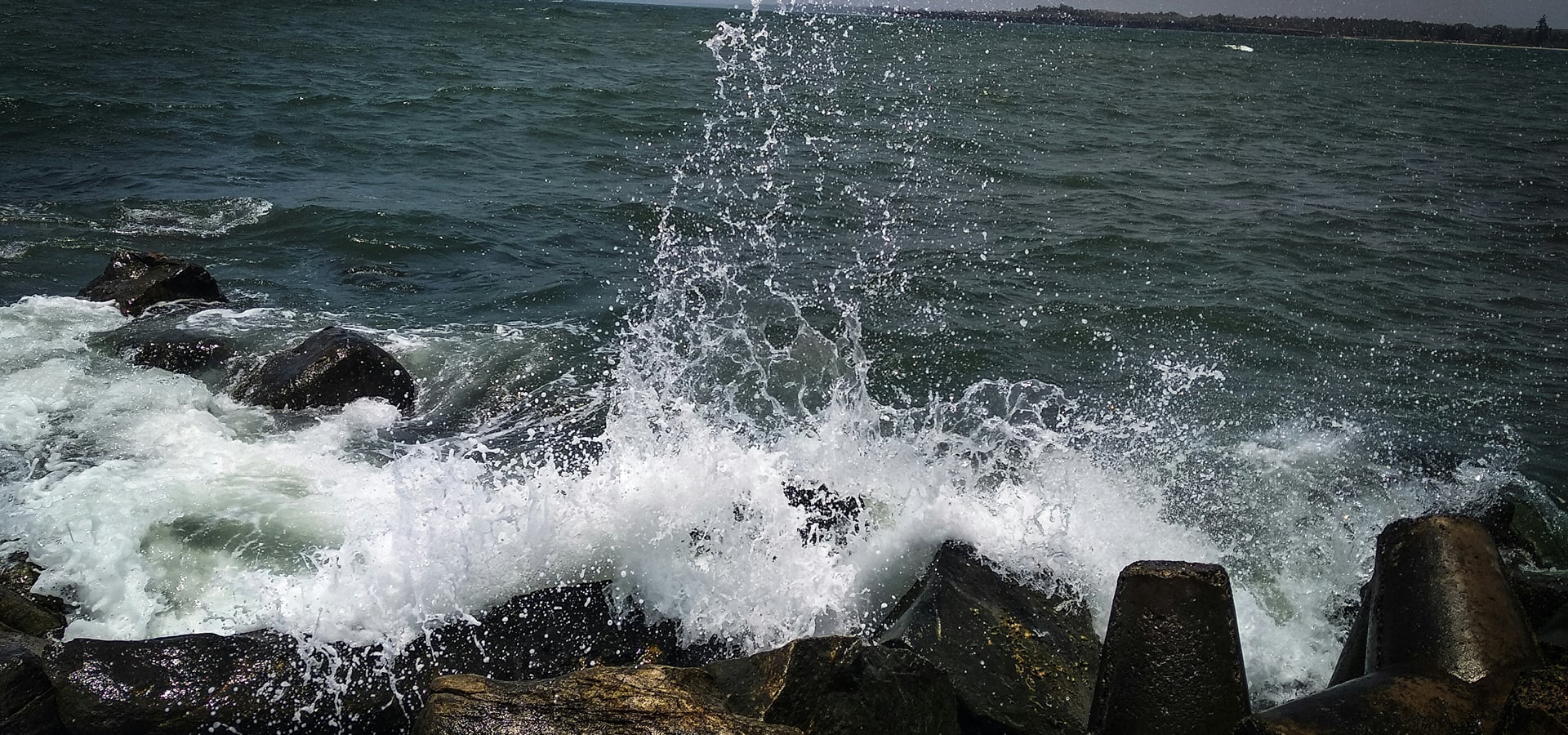 Waves breaking in white spray over dark rocks along the shore | Shirgaonkar Beach Resort
