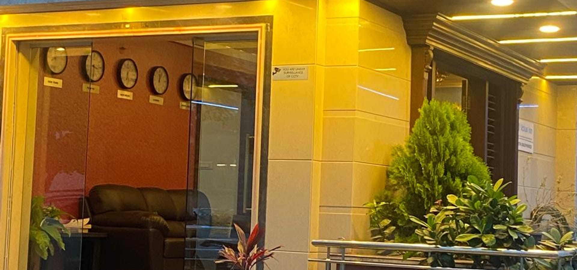 Brightly lit entrance of Value Inn, Bangalore Airport at night with a glowing blue name board, warm lighting, and potted plants by the door