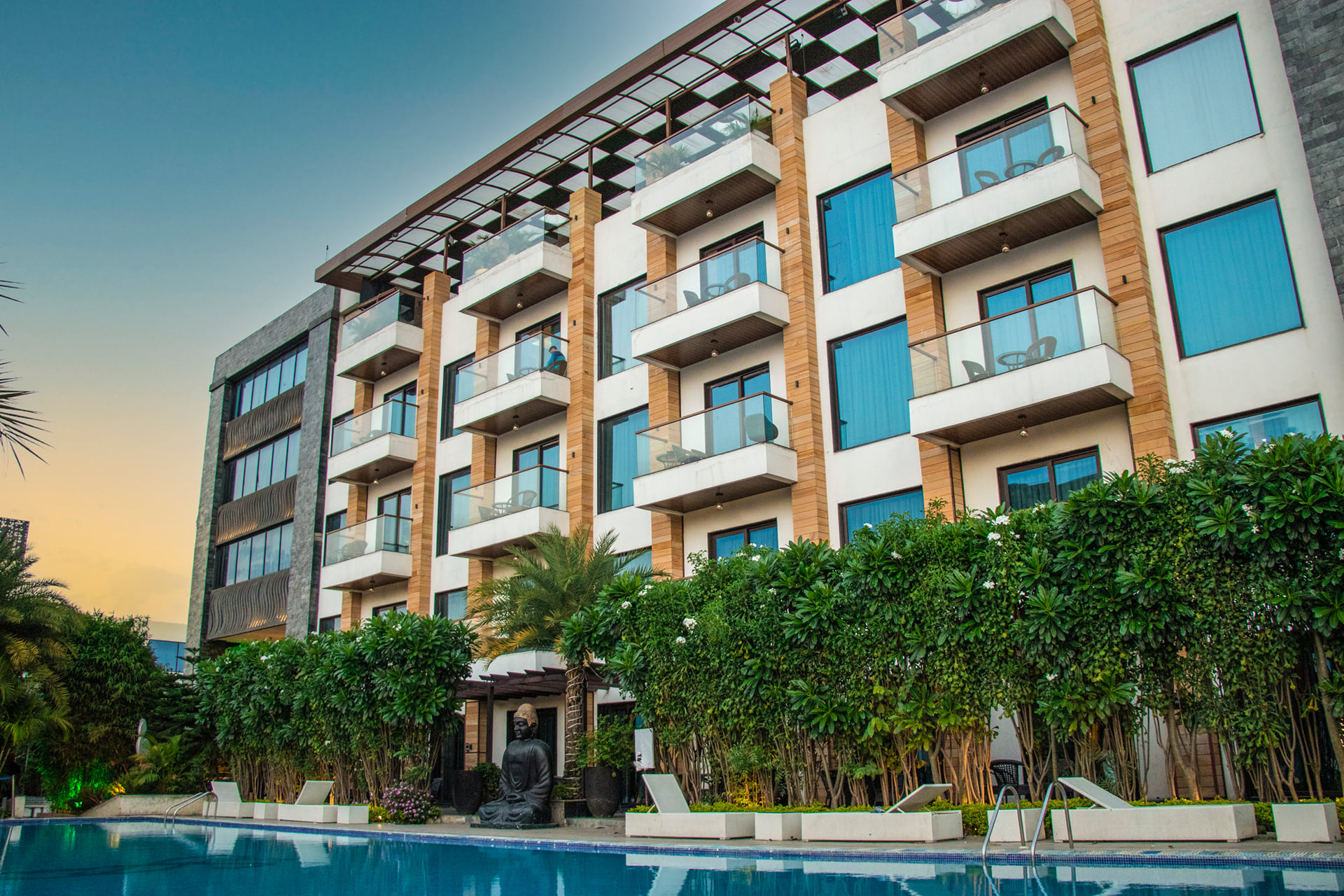 Skyline by Miraya hotel facade with balconies and blue-glass windows, framed by hedges and palms at sunset
