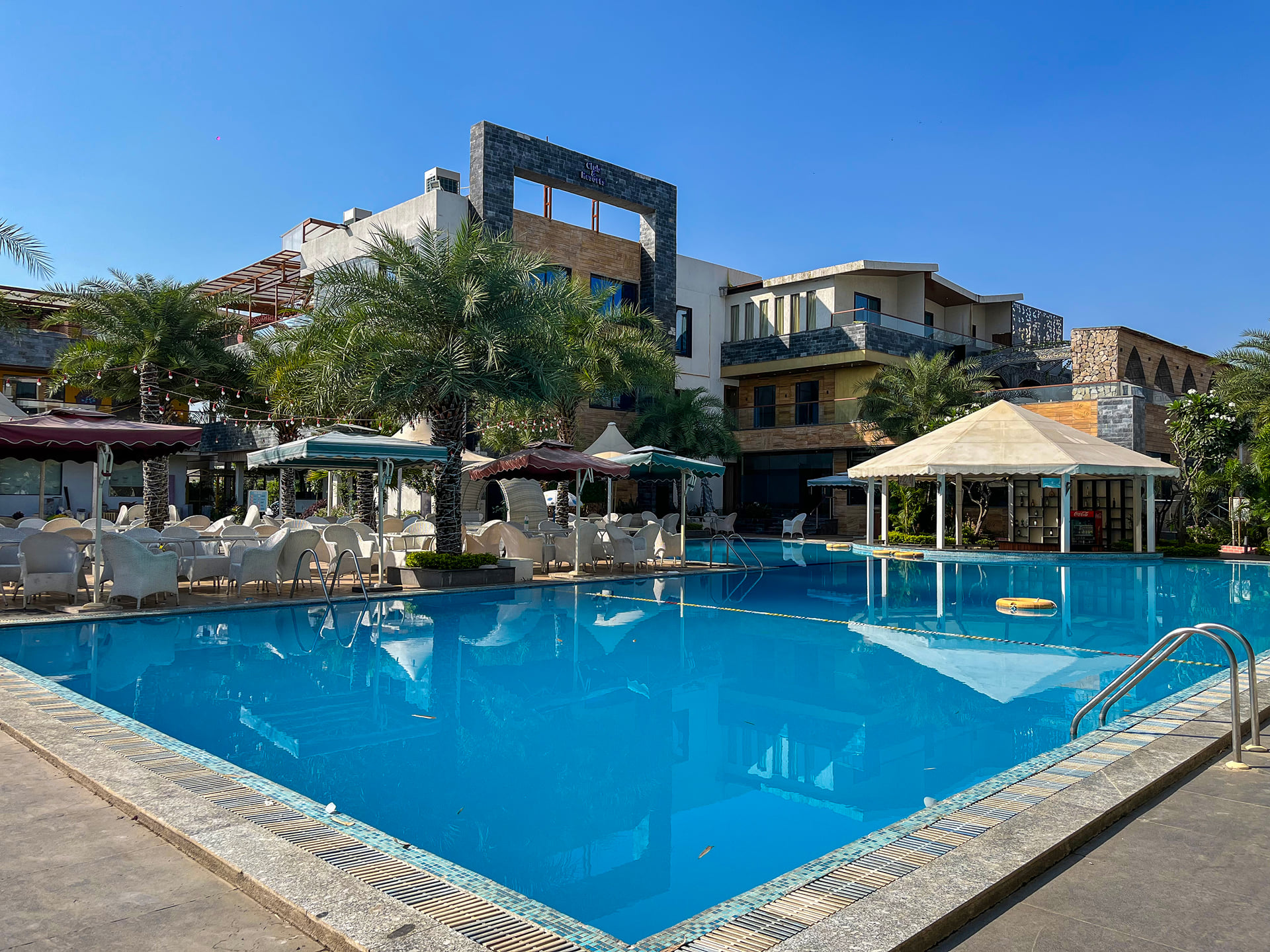 Swimming pool with a white gazebo on the far side, sun loungers and the hotel building under a blue sky