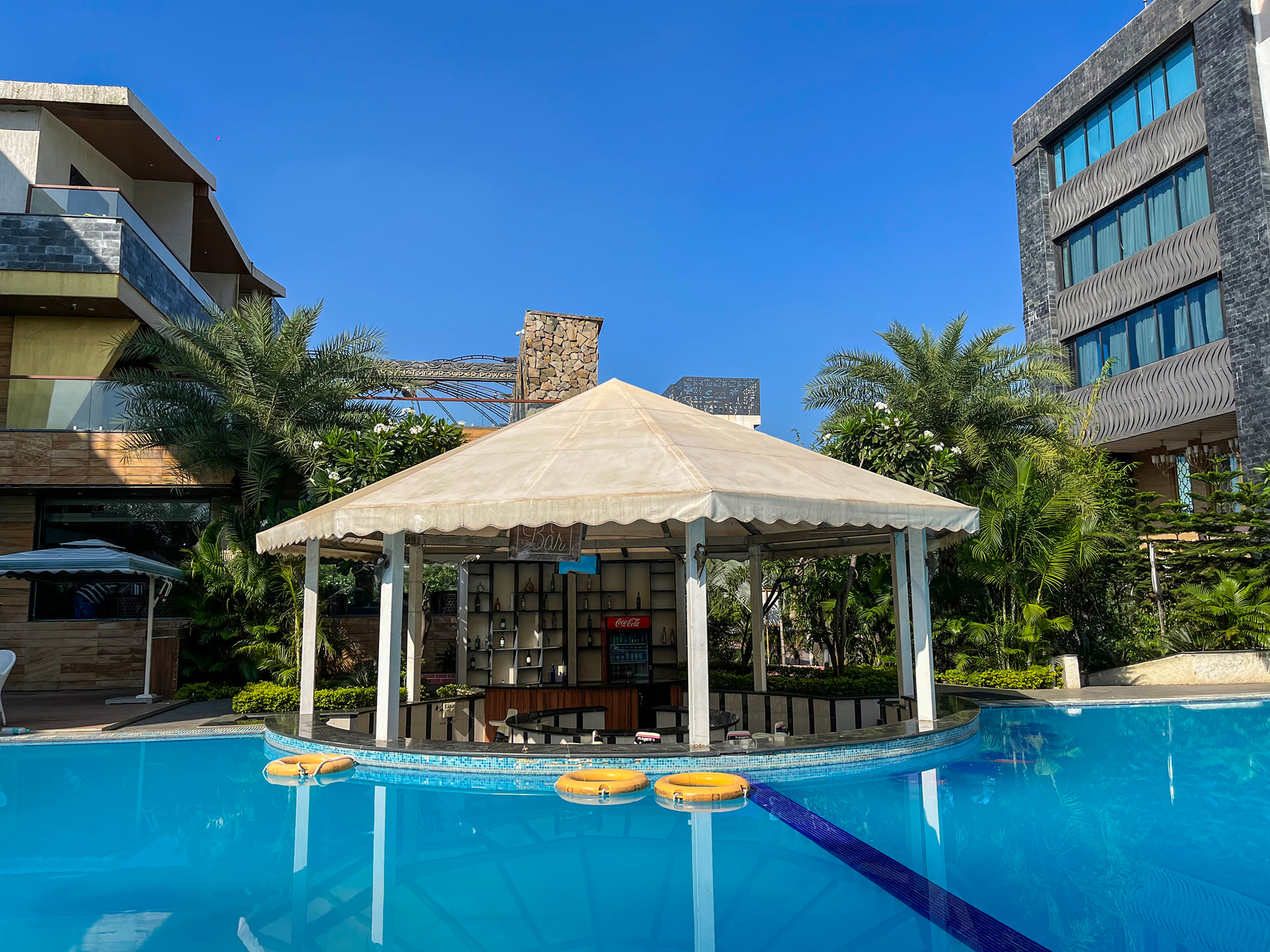 White poolside gazebo with floating rings in the swimming pool, palm trees and the hotel behind
