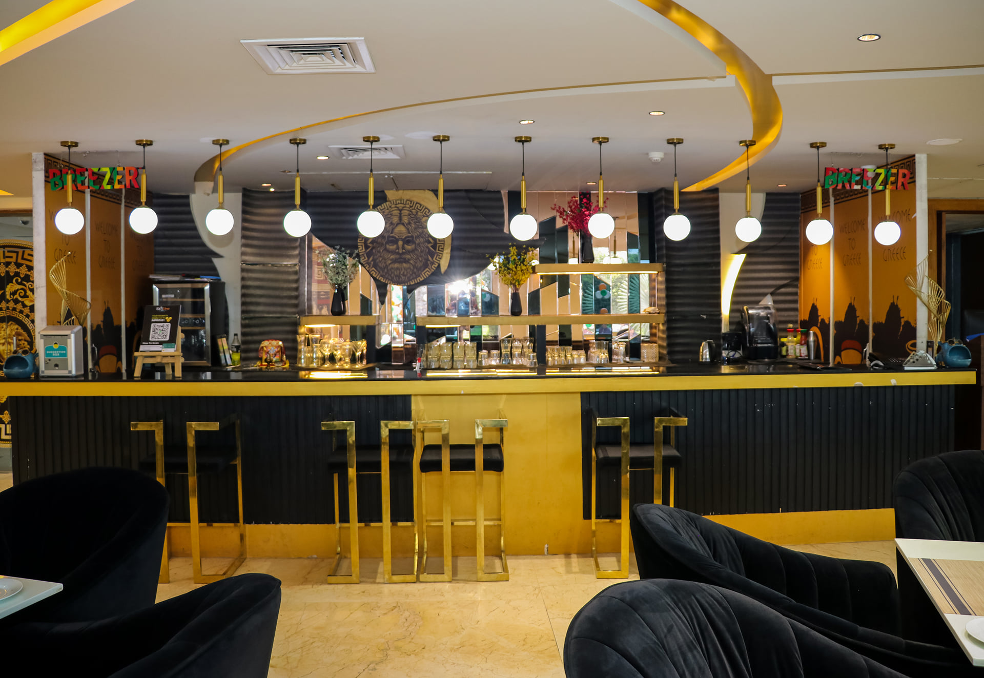 Zeus restaurant bar counter with gold pendant lights, tall stools and black velvet chairs in the foreground