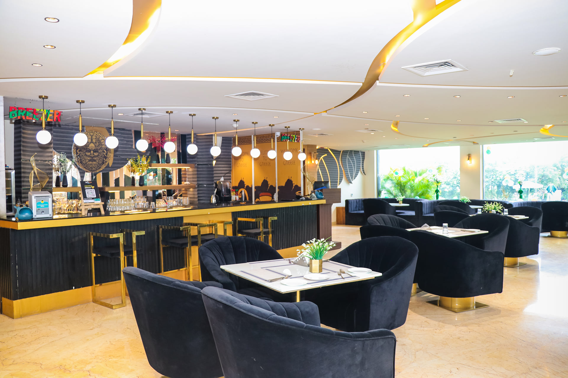 Zeus restaurant dining room with black velvet armchairs, white tables and a gold-trimmed bar with pendant lights