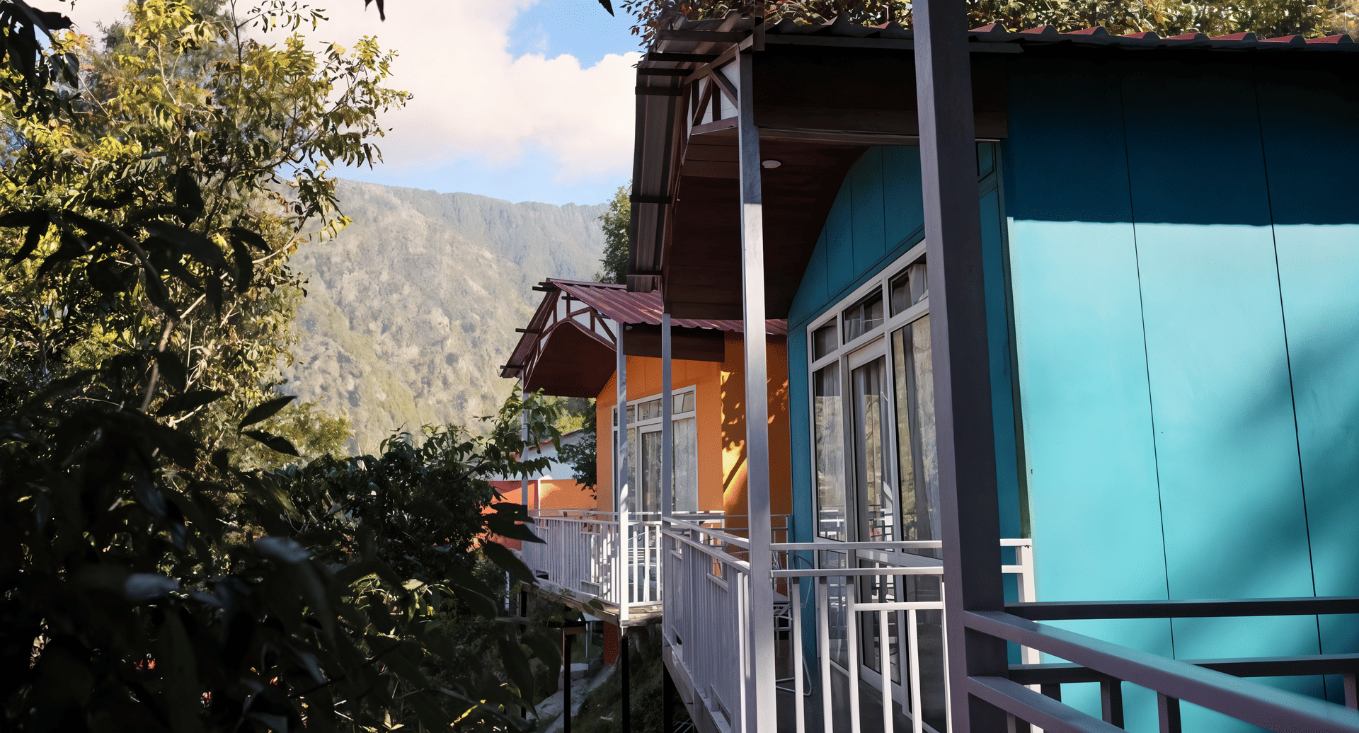 Balcony walkway lined with teal and orange cottage doors at Nazaara Nature Retreat, mountain views in daylight, Dalhousie