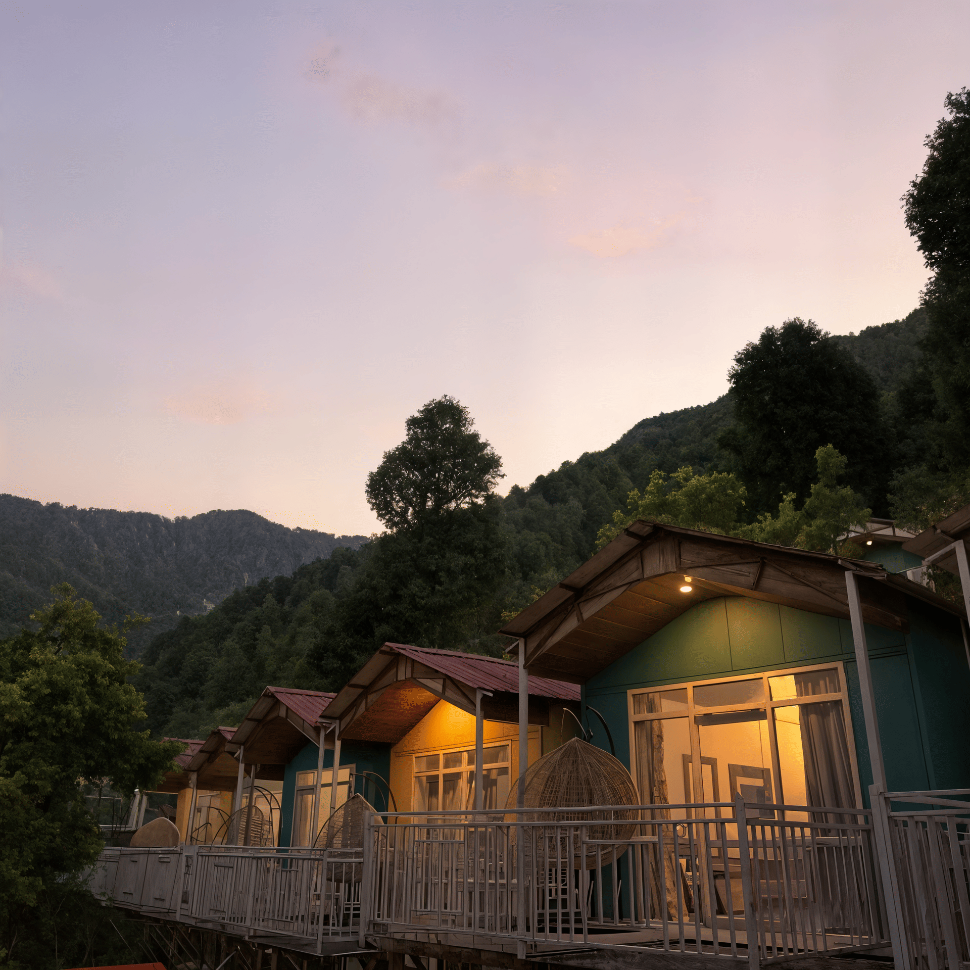 Nazaara Nature Retreat's timber cottages along a wooden boardwalk, pine forest silhouetted behind them at twilight, Dalhousie