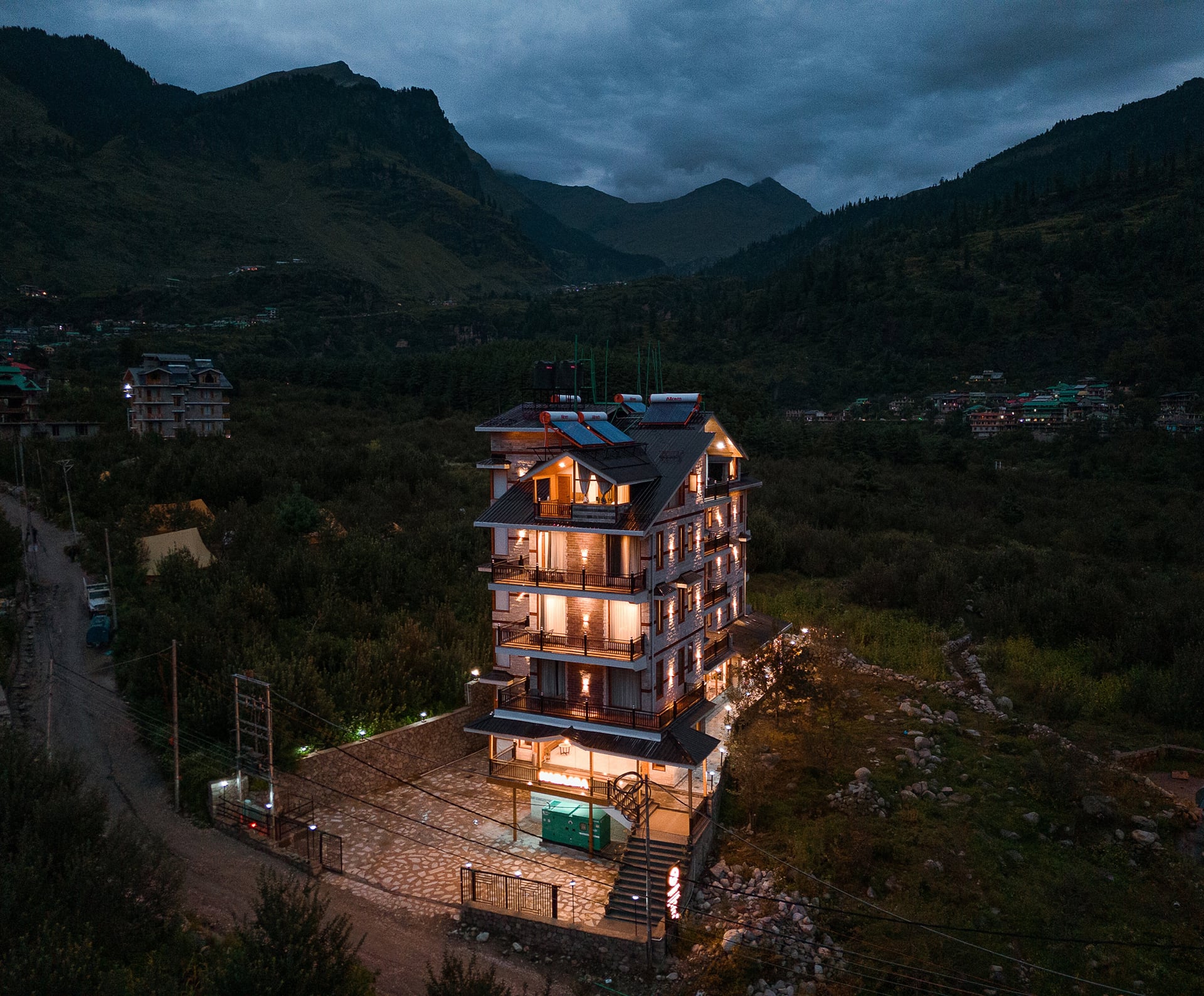 Aerial drone view of Nazaara Luxe Retreat lit up at night, the dark silhouette of the mountains all around, Manali