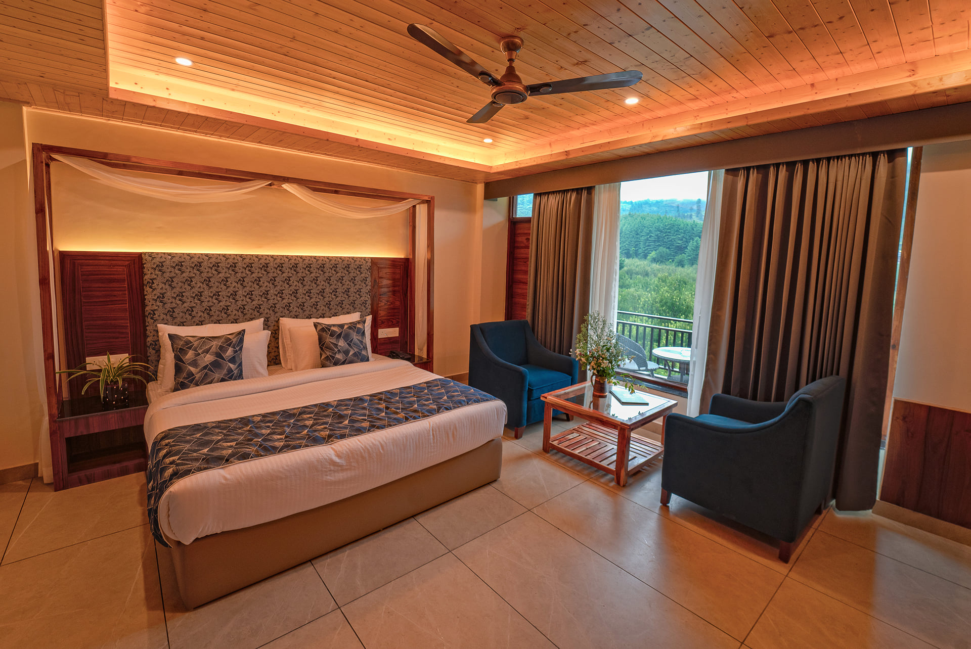 Bed and armchairs in a Luxurious Room at Nazaara Luxe Retreat, forest filling the window, Manali