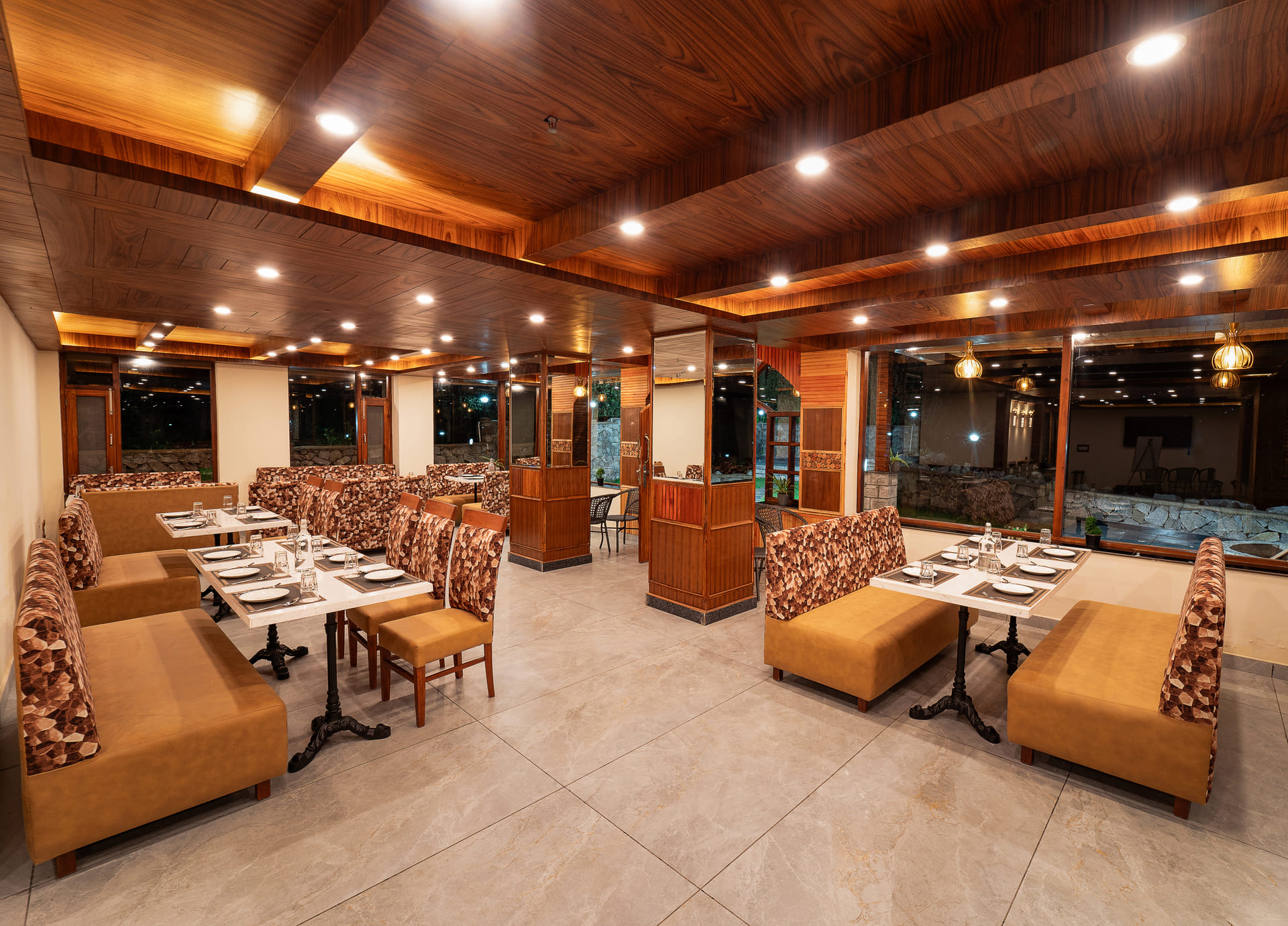 Wide interior view of Restro & Café at Nazaara Luxe Retreat, rows of wooden tables and chairs in a rustic dining room