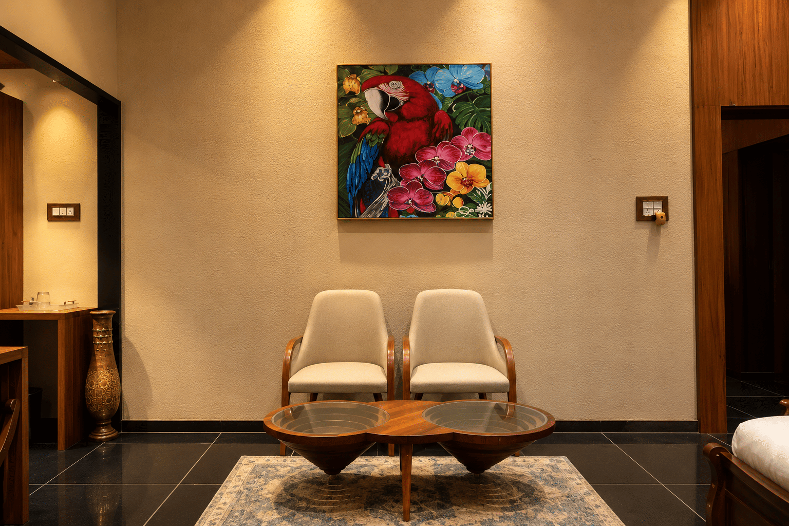 Two cream armchairs and a round teak table beneath a bright painting of macaws at The Garud Forest, Tadoba