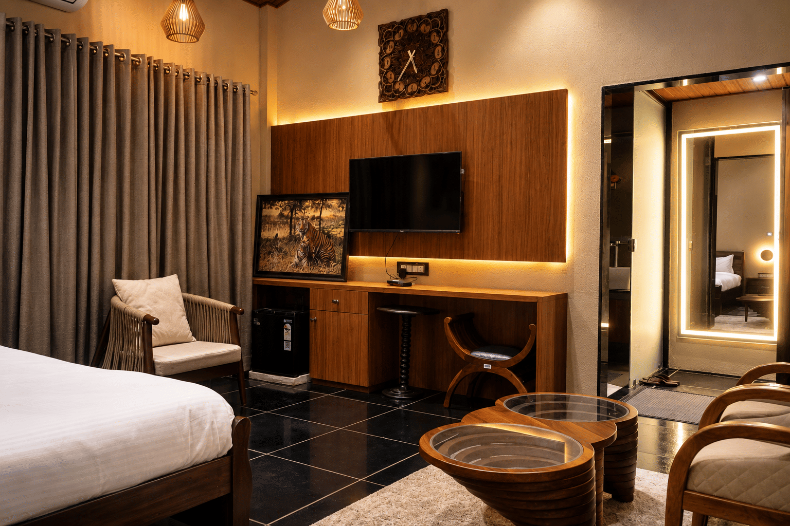 A work desk and television console in teak beside a backlit mirror in a guest room at The Garud Forest, Tadoba