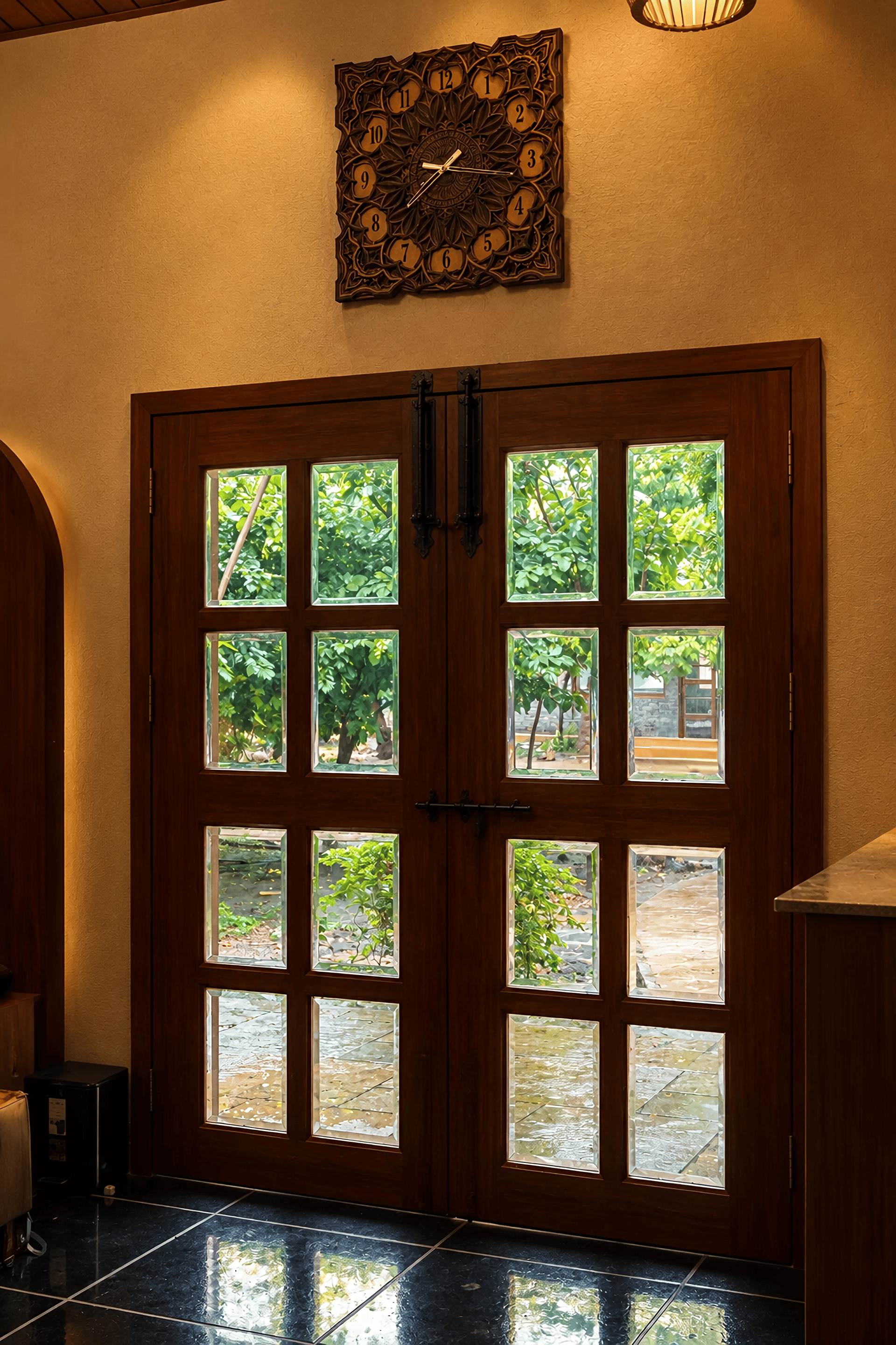 Wooden French doors opening onto greenery beside a carved wall clock in the lobby of The Garud Forest, Tadoba