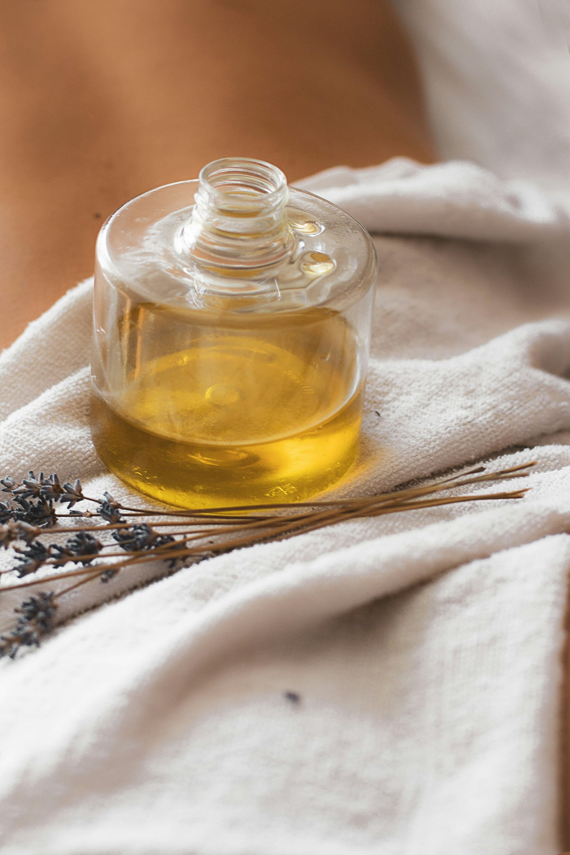 A glass bottle of golden massage oil resting on white linen beside dried lavender in the spa at The Garud Forest, Tadoba