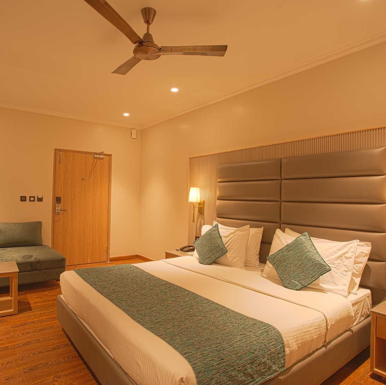 a double bed with a ceiling fan and lounger on the side inside Pool view room - The Cindrella Hotel, Siliguri