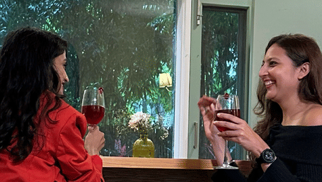 Two women sitting across near the counter table, drinking and chatting amongst each other.