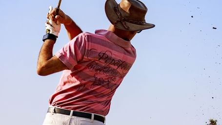 Golfer in mid-swing hitting a shot on the golf course under clear skies at Karma Chalets.