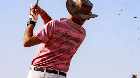 A man wearing a hat on a lawn playing golf under a clear sky at Karma Chalets