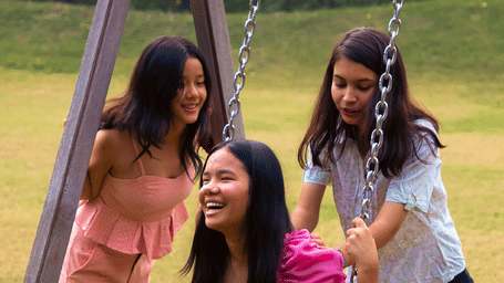 A girl on a wooden swing held by another girl behind her and the other girl smiling at Karma Chalets