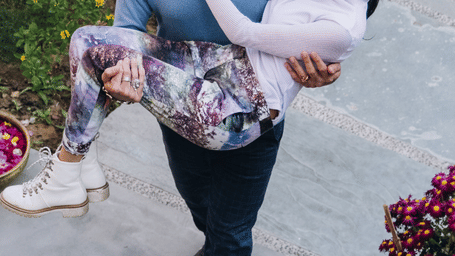 A man wearing sunglasses, lifting a woman in his arms outdoor next to flowers at Karma Chalets