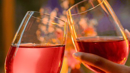 2 hands clinking 2 glasses with beverages outdoor as the sunlight illuminates the beverage's colour at Karma Chalets