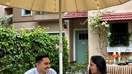 Couple enjoying an outdoor garden dining experience under a lit umbrella at Karma Chalets, with beverages, floral table setup, and cosy evening ambiance.