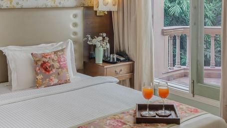 Guest room featuring floral wallpaper, bed with decorative runner, and balcony overlooking gardens at Karma ChaletsRetryClaude can make mistakes. Please double-check responses.