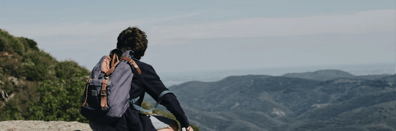 A man sititng on a rock on  a hilltop looking at the mountains in front of him