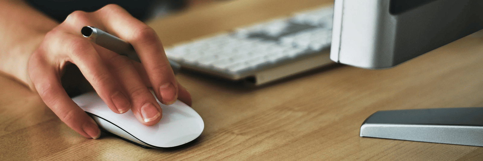 A person holding a mouse and standing in front of the computer
