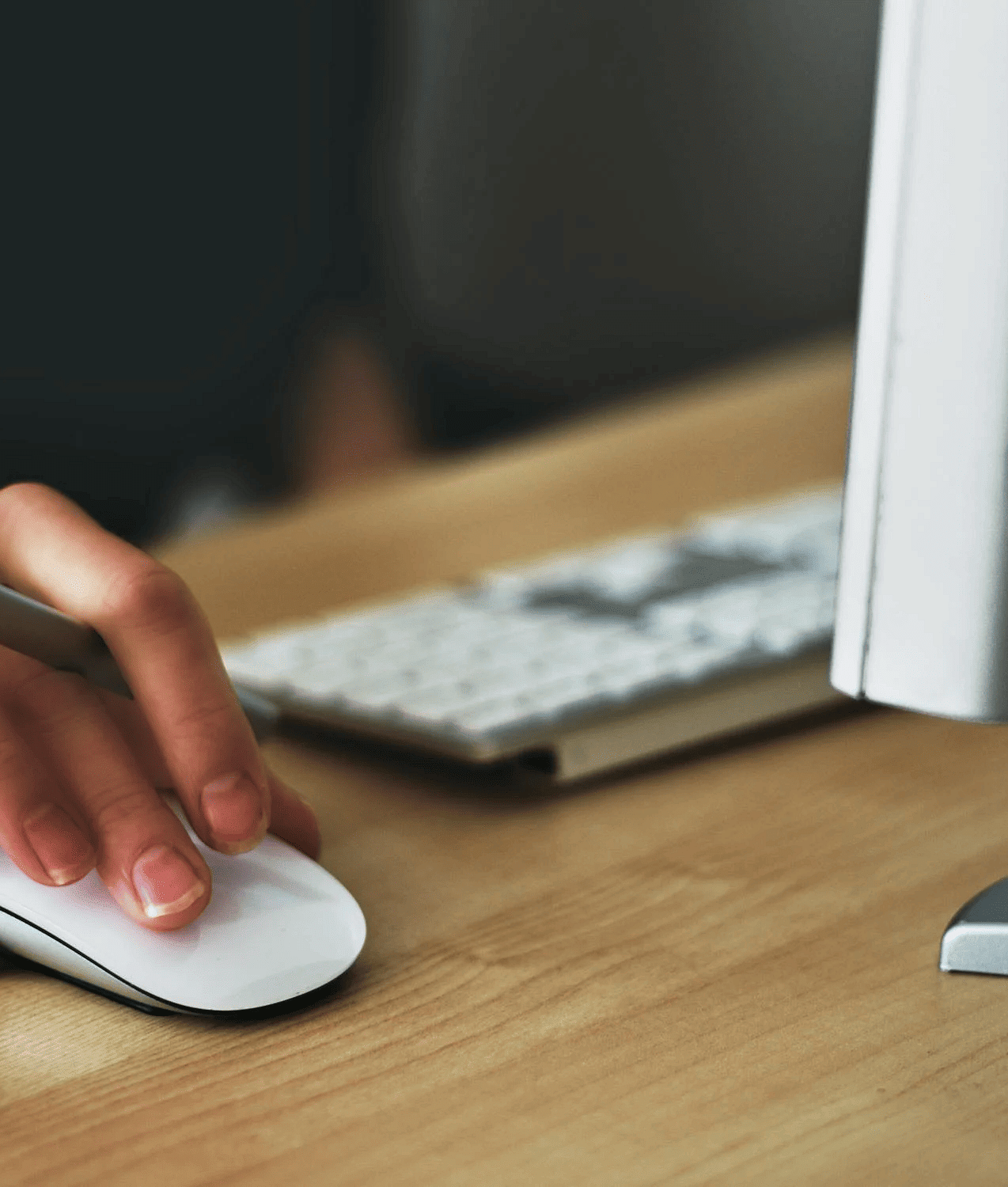 A person holding a mouse and standing in front of the computer