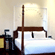 A room with a large bed, spreads, pillows, a fan, and a table. | Hotel Devnadi, Haridwar