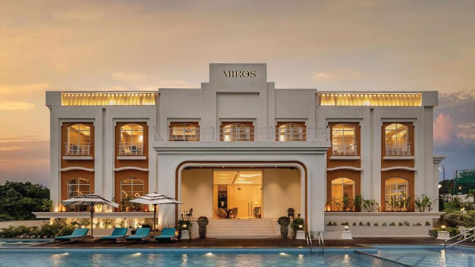 Full view facade of Miros Hotels with a calm swimming pool in the foreground along with beautiful sunset skies in the background.