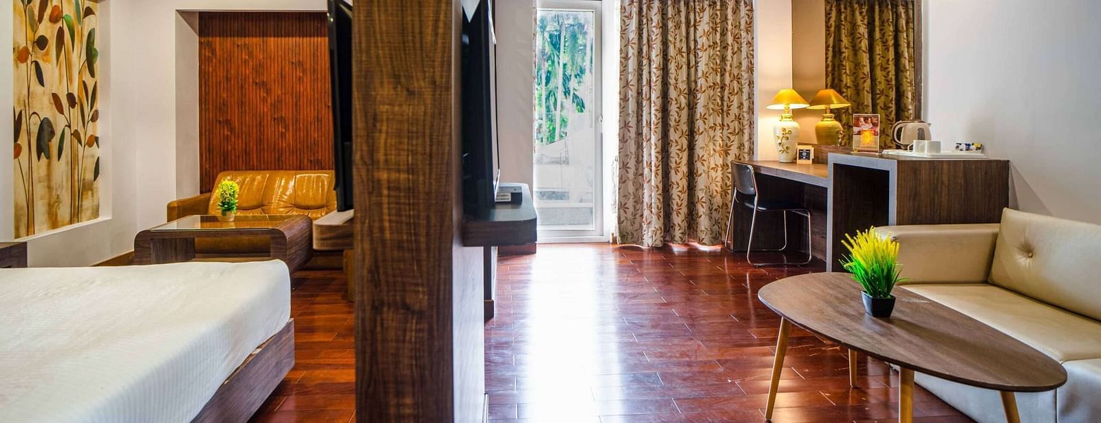 A room with a bed on side of the partition and the other side showcases a sofa, a coffee table, and more amenities at Mansha Hotel Regency.