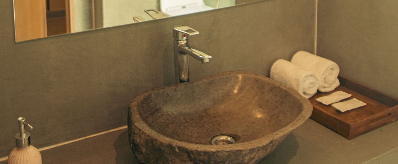 Bathroom with a circular basin on a stone counter, mirror, and a glimpse of the toilet at Fireflies Resorts, Kabini.