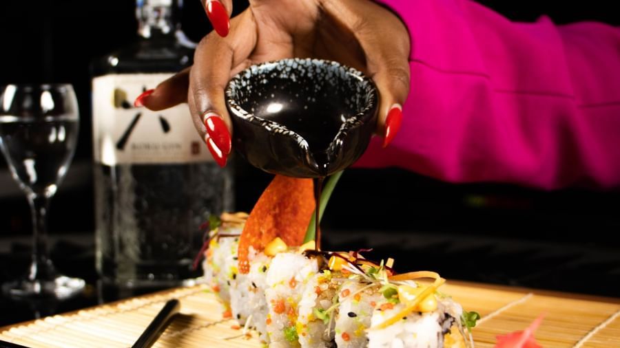A person pours a drink from a shaker at Asiatic Lounge, with plates of food and drink garnishes on a wooden counter