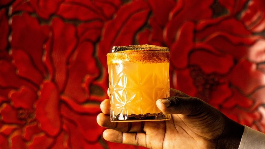 Hand holding a drink served in a glass placed in front of a round red plate at Asiatic Lounge.