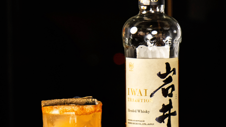 Bottle placed next to a glass filled with a drink on a reflective surface at Asiatic Rooftop Bar and Restaurant.
