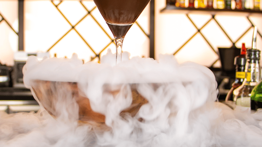 A close view of a glass bowl with dry ice placed on a bar counter, cocktail glass positioned on the bowl at Asiatic Rooftop Bar and Restaurant.