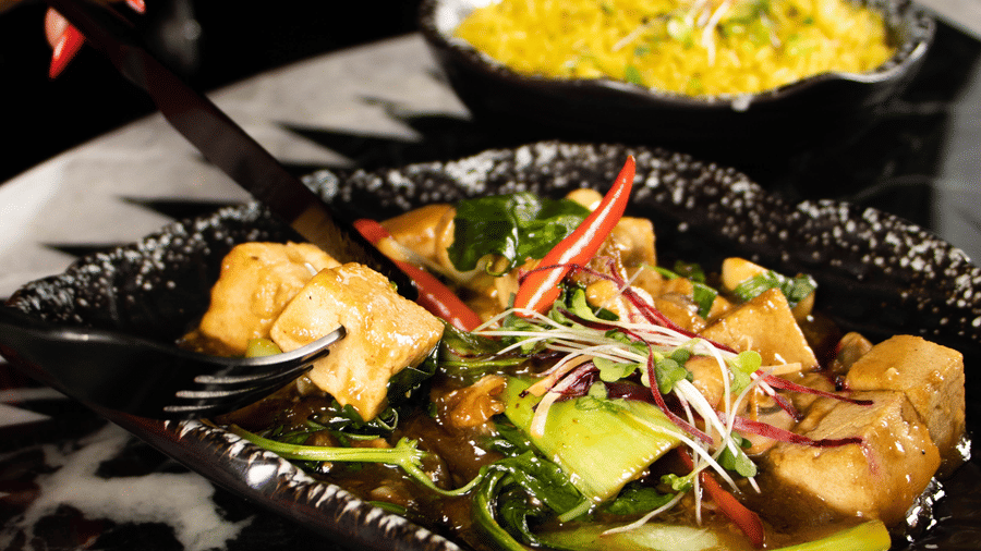 Plate with food items being served, with a hand holding a spoon at Asiatic Rooftop Bar and Restaurant.
