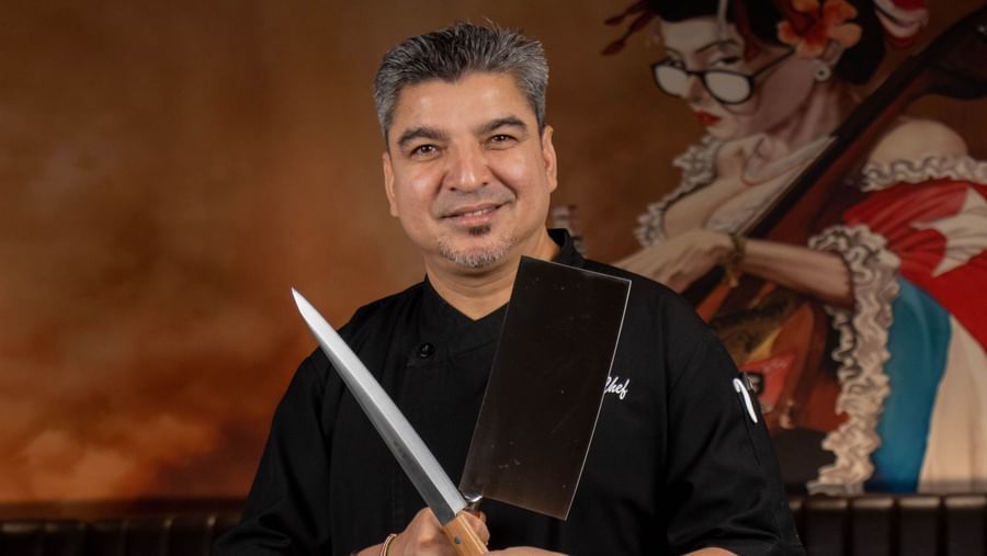 Chef stands holding knives in front of restaurant seating at Asiatic Lounge.