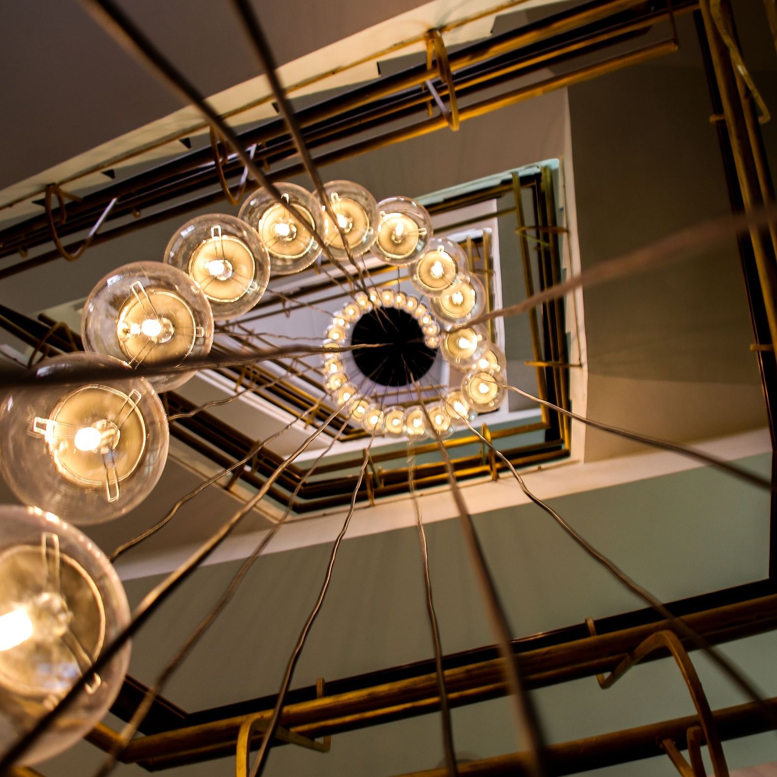 View from below of a spiral staircase with a chandelier of round lights | T24 Retro