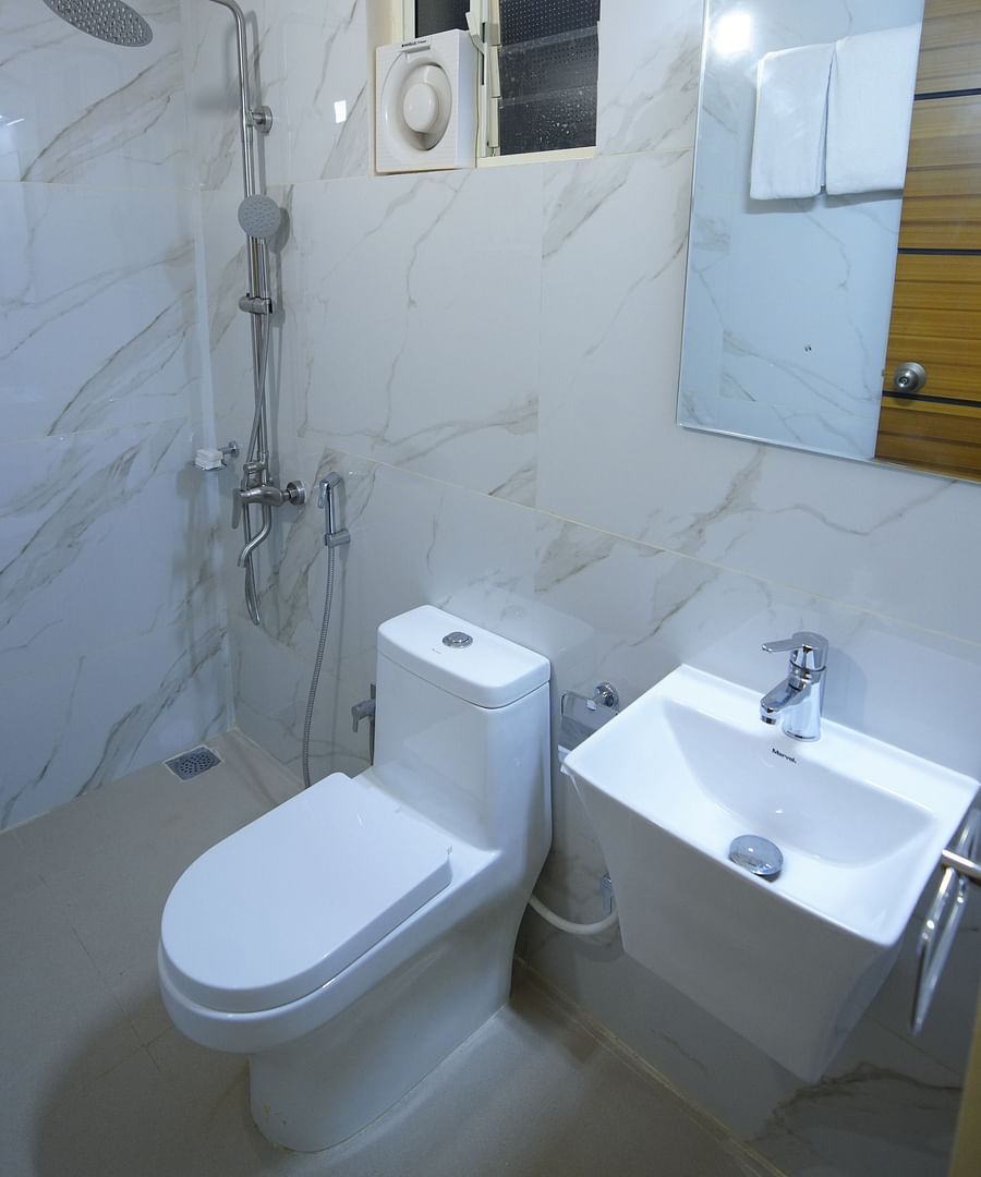 Bathroom of the accommodation in GK Hill View Resort furnished with a sink, western commode, wall-mounter heater, exhaust and shower fittings.