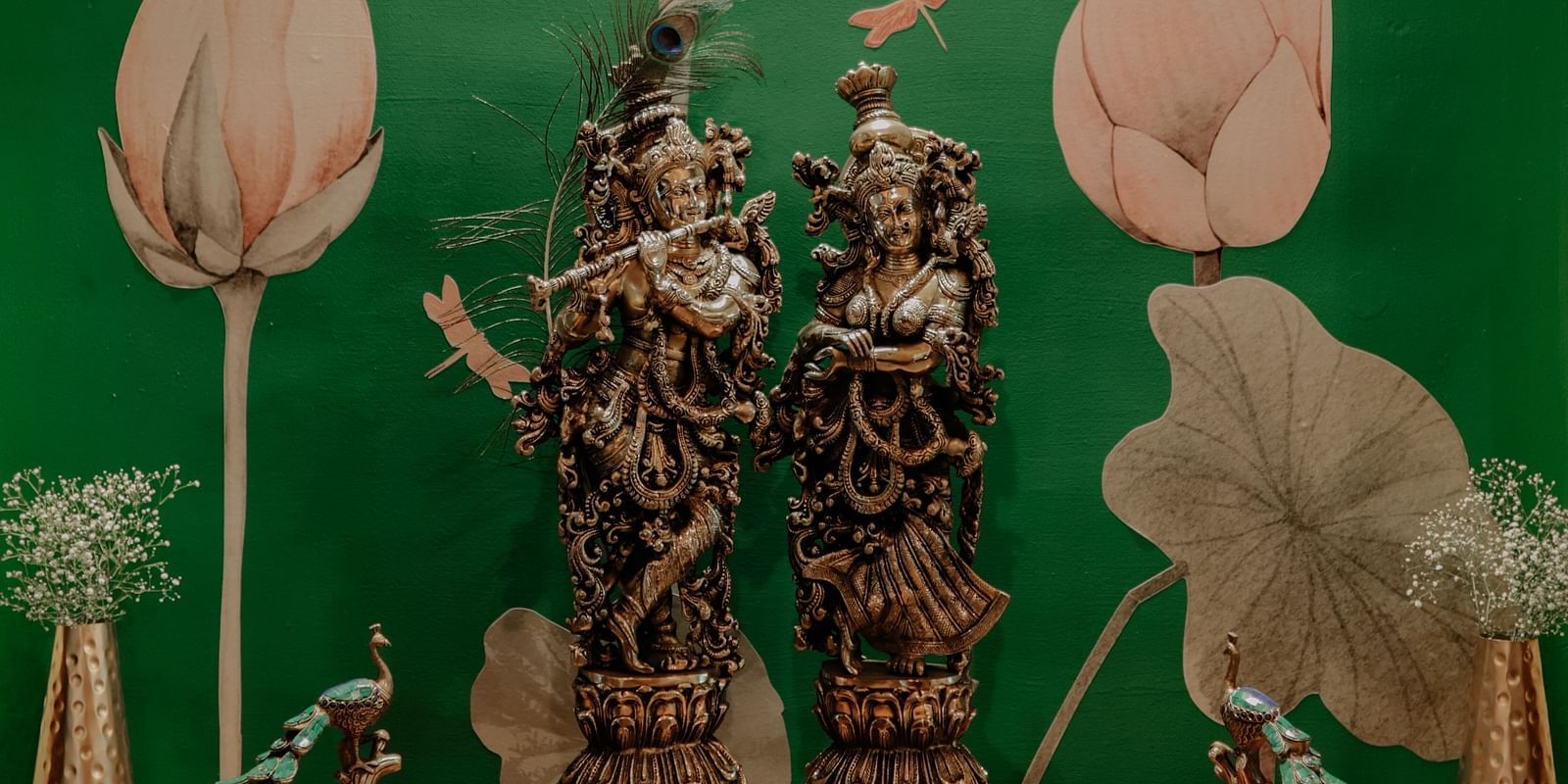 Two ornate statues under a spotlight in front of a green wall with lotus designs | Adhyaya Heritage Reverbed