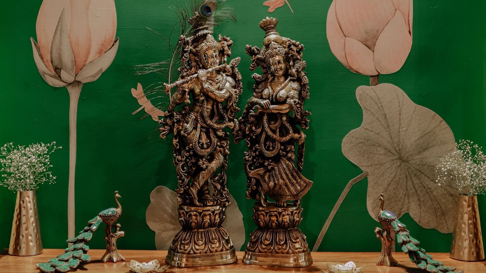 Two ornate statues under a spotlight in front of a green wall with lotus designs | Adhyaya Heritage Reverbed