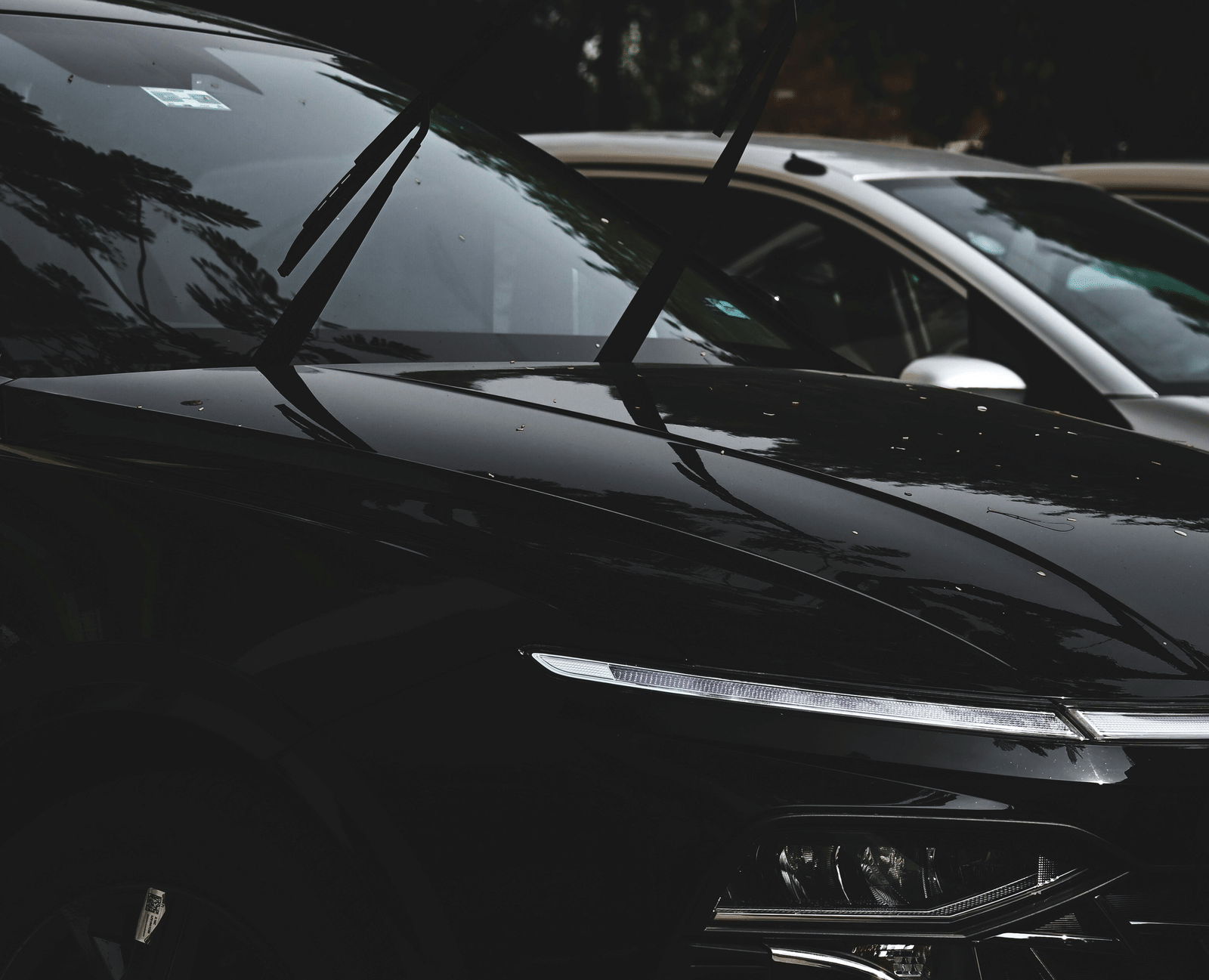 A black car parked outdoors with part of another vehicle visible in the background.