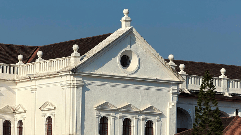 The white facade of a colonial-style building with a triangular pediment, set against a clear blue sky in Old Goa.