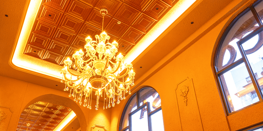 Elegant indoor dining hall at Cocobrisa featuring grand chandeliers, high ceilings with wooden detailing, large arched windows, modern seating, and a warm ambient setting for guests.
