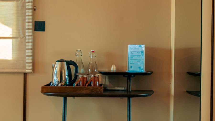 A corner with mounted lamp, a table with kettle, cups, and bin below at Fireflies Resorts, Kabini.
