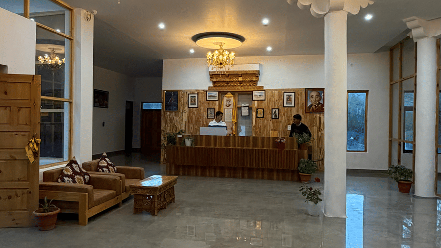  A space with  chandeliers, wooden sofas, elongated desk with people standing by it at the reception. | Indus Serinity, Leh Ladakh