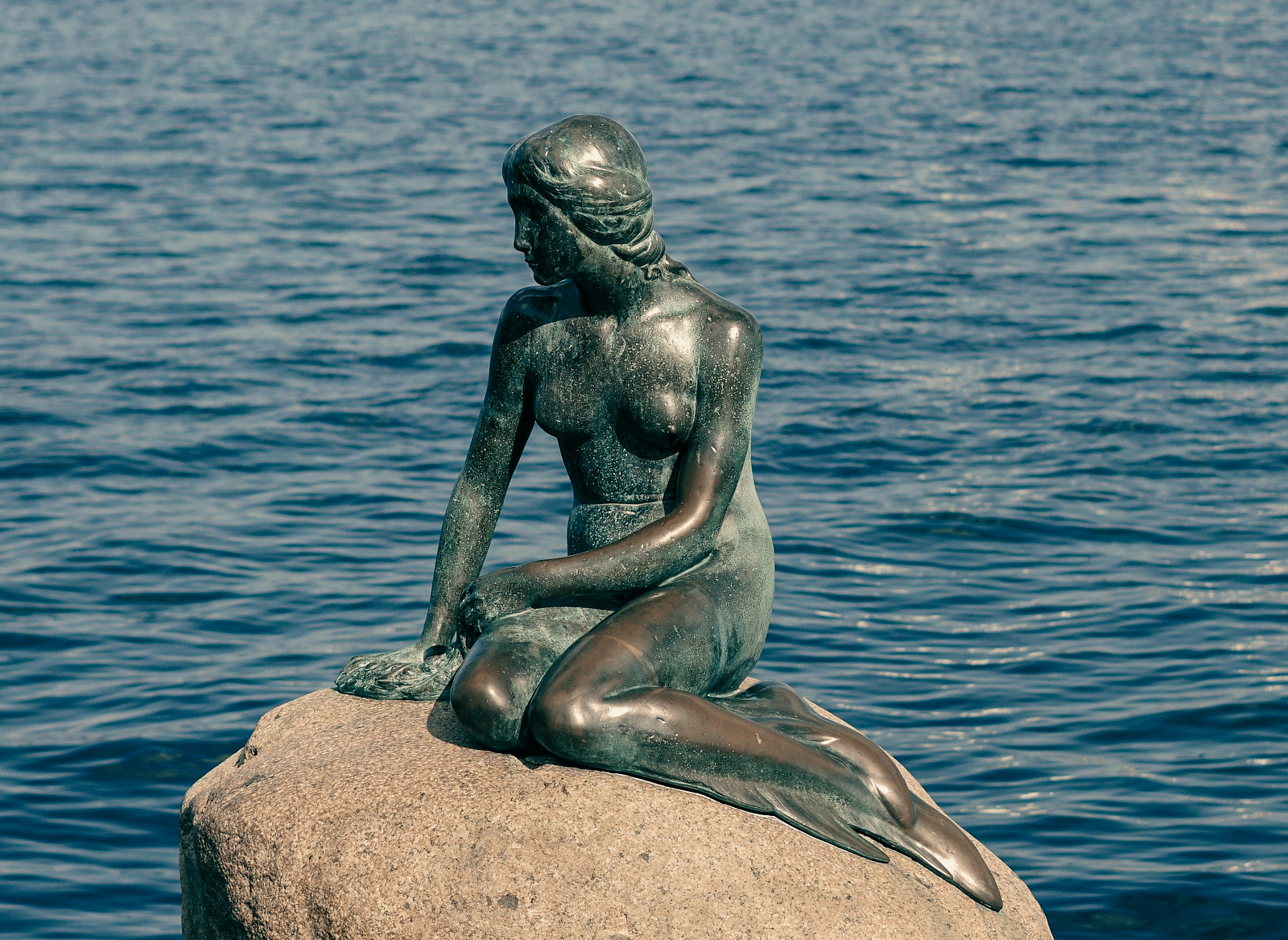 A statue of mermaid made with a lake in the background