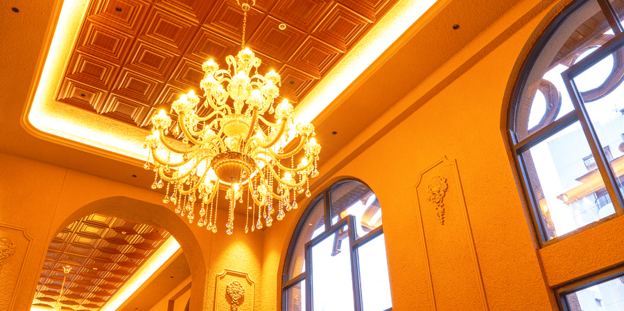 Elegant indoor dining hall at Cocobrisa featuring grand chandeliers, high ceilings with wooden detailing, large arched windows, modern seating, and a warm ambient setting for guests.