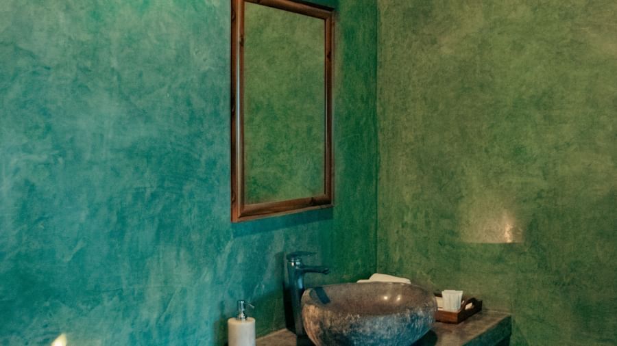 Bathroom with green walls, a vessel sink, mirror, and toiletries on a stone counter at Fireflies Resorts, Kabini.